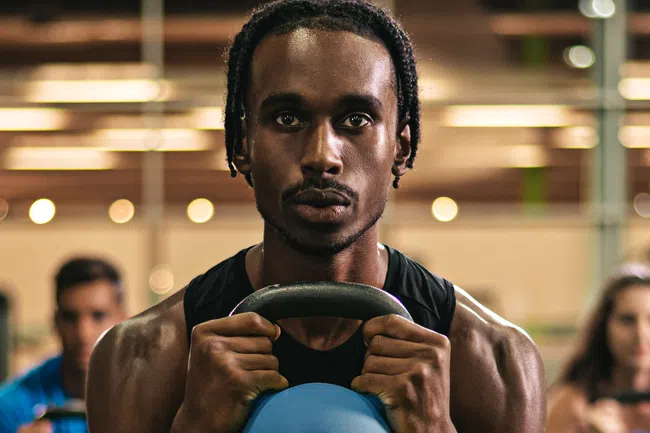 Determined man lifting a kettlebell during a gym workout with blurred people and lights in the background