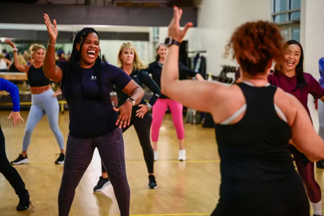 Diverse group of women enjoying a lively dance fitness class in a bright gym studio.