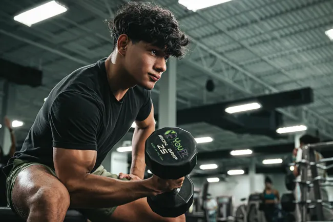 Young man with curly hair lifting a 25-pound dumbbell in a modern gym setting focused on strength training.