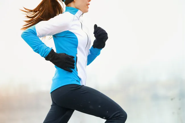 Woman running outdoors in winter gear with gloves and a blue and white jacket on a cold day