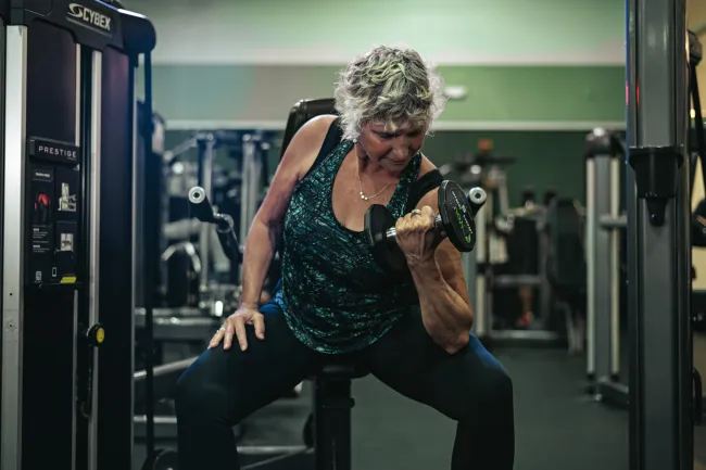 Mature woman lifting a dumbbell seated on gym equipment focusing on strength training.
