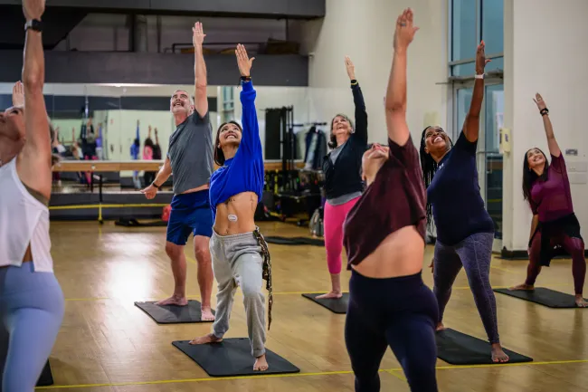 Group of diverse adults practicing yoga poses in a bright studio with wooden floors and mirrors.