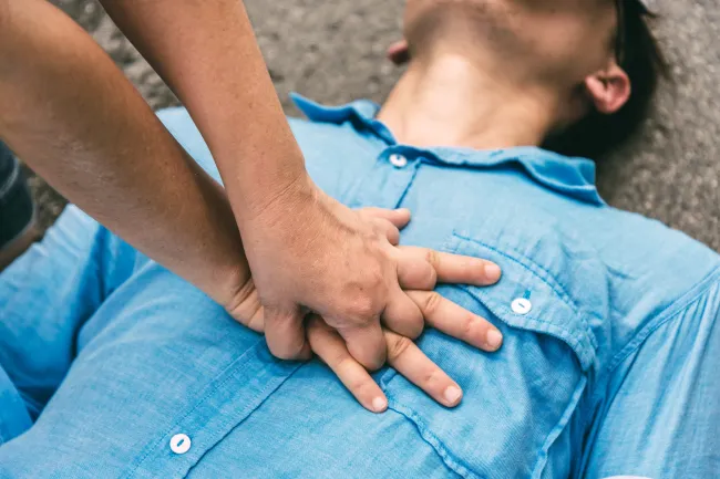 Close-up of hands performing CPR chest compressions on a person lying on the ground wearing a blue shirt