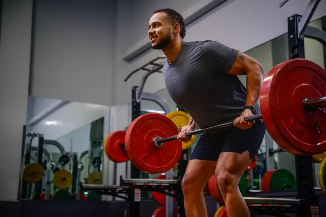Man lifting a barbell with red weights in a gym, focused on strength training and fitness.