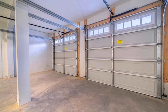 Empty two-car garage with closed white sectional doors and concrete floor under bright lighting