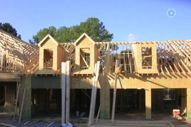 Wooden house frame under construction with roof trusses and dormer windows on a clear sunny day.