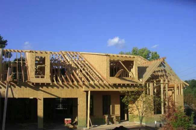 Partially framed house under construction with exposed wooden beams and clear blue sky background.