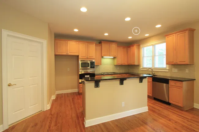 Bright kitchen with wooden cabinetry, black countertops, stainless steel appliances, and hardwood floors in a modern home.