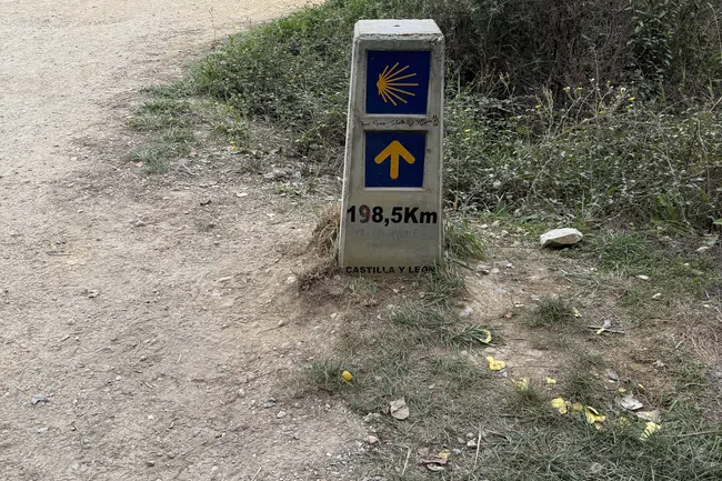 Stone marker on dirt path showing 198.5 km to Santiago de Compostela in Castilla y León on Camino de Santiago trail.