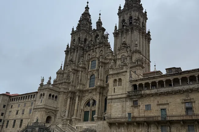 Crowd of tourists visiting the grand historic cathedral with intricate stone facade and twin spires on cloudy day.