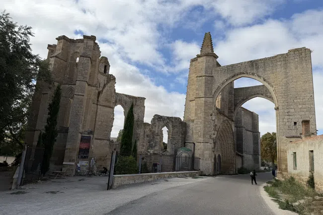 Ancient stone ruins with large arches and gothic windows under a cloudy sky beside a curved road.