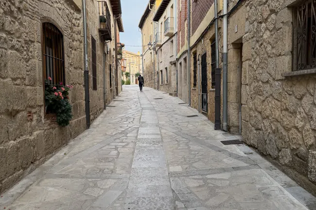 Narrow cobblestone street lined with stone and brick buildings under an overcast sky in a European village.