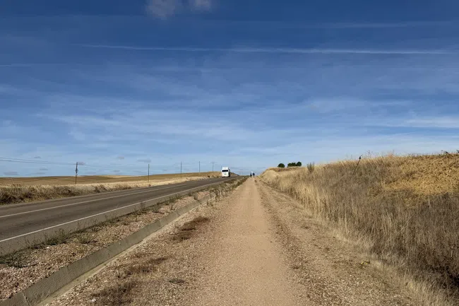 Gravel walking path parallel to a rural road under a clear blue sky with dry grass on the sides.