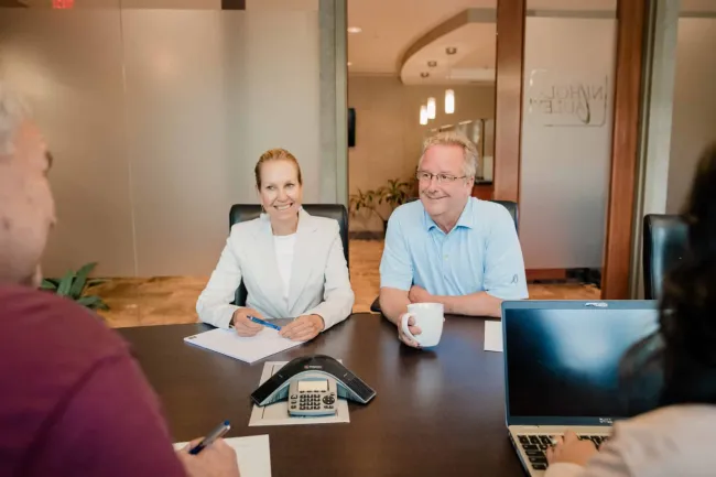 Business meeting with four professionals discussing notes, laptop, and phone conference in modern office.