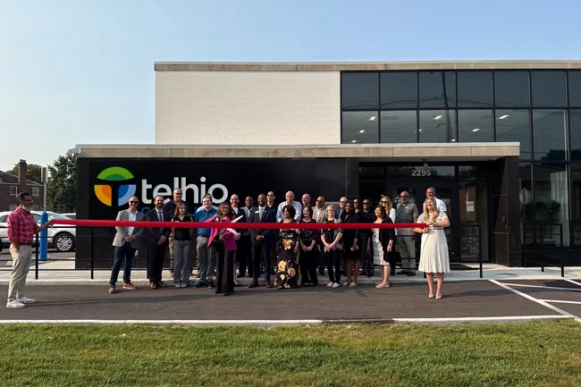Group of people cutting a red ribbon at the Telbio office building grand opening event on a sunny day.