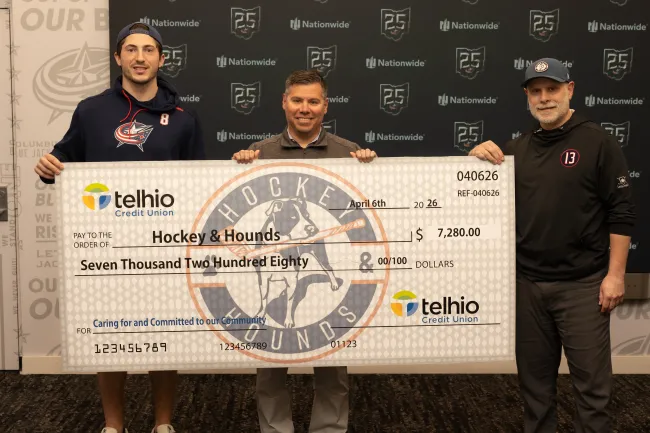 Three men holding a large $7,280 donation check from Telhio Credit Union to Hockey & Hounds on April 6th, 2026.
