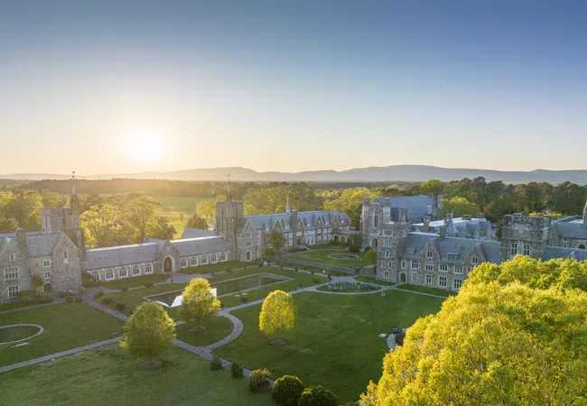Aerial view of a picturesque college campus at sunrise, showcasing historic buildings and lush greenery.