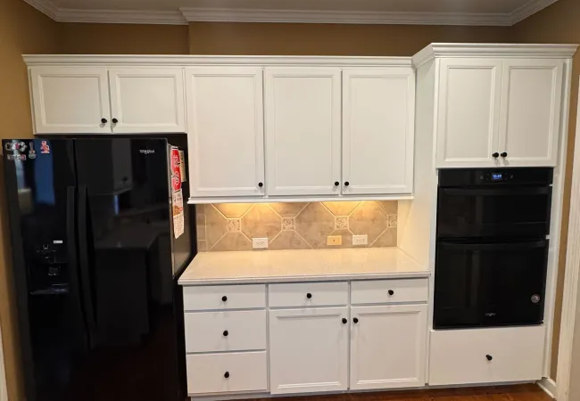 Modern kitchen with white cabinets, black appliances, tile backsplash, and wood flooring under recessed ceiling lights