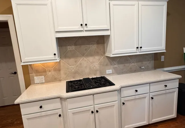 Modern kitchen with white cabinets, beige tiled backsplash, black cooktop, and hardwood floor