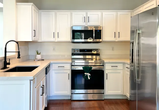 Modern kitchen with white cabinets, stainless steel appliances, dark wood floor, and black faucet under recessed lighting.