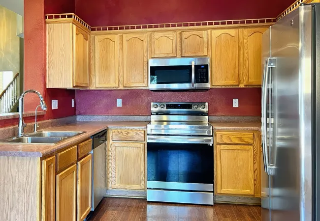 Modern kitchen with oak cabinets, stainless steel appliances, maroon walls, and hardwood flooring.