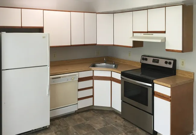 Compact kitchen with white cabinets, wood countertops, stainless steel oven, white fridge, and dishwasher.