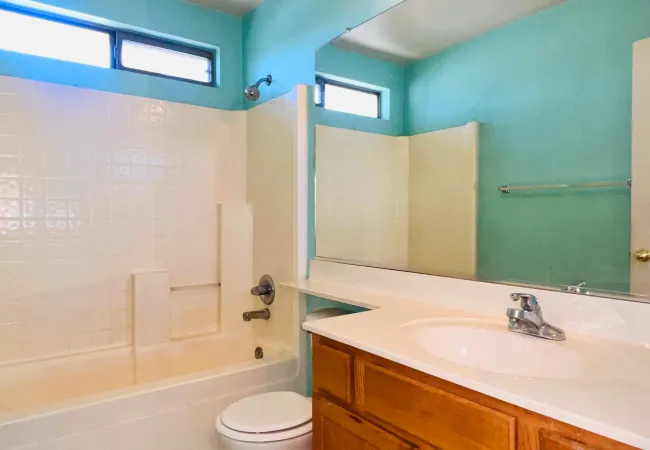 Clean bathroom with white bathtub, toilet, wooden vanity, large mirror, and turquoise walls.