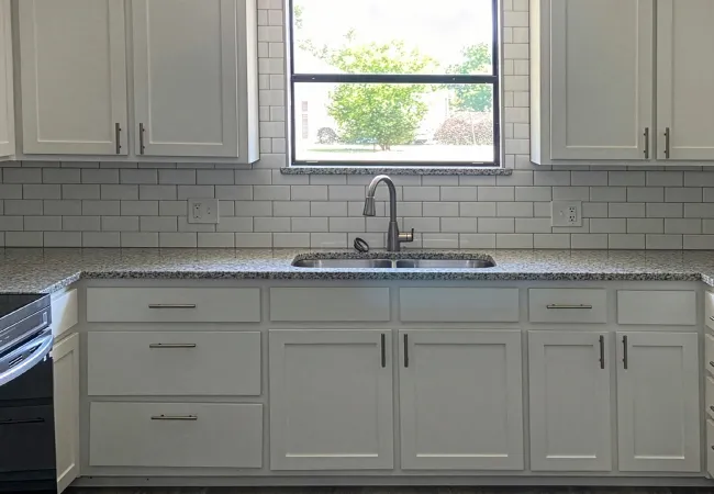 Modern kitchen with white cabinetry, granite countertops, stainless steel appliances, subway tile backsplash, and window.