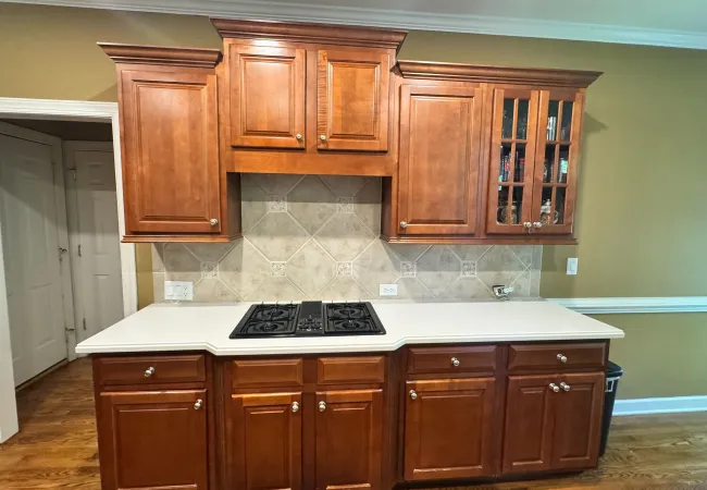 Modern kitchen with cherry wood cabinets, white countertop, gas stove, and beige tile backsplash under bright lighting.