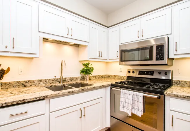 Bright modern kitchen with white cabinets, granite countertops, stainless steel stove and microwave, and double sink.