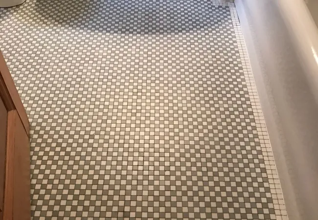 Bathroom floor with vintage black, white, and gray checkered tile pattern next to white porcelain bathtub and toilet.