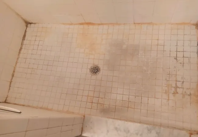Before photo of Dirty white tiled shower floor with stained grout and central drain visible.