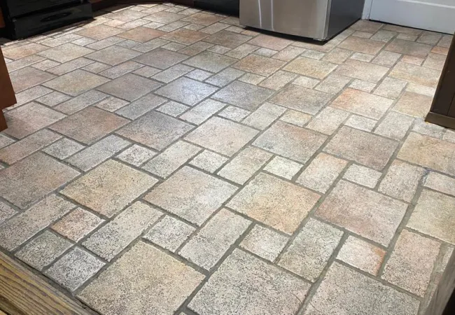 Close-up of square and rectangular ceramic floor tiles in beige and gray tones in a kitchen setting.