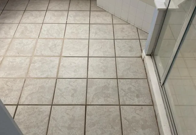 Bathroom floor with beige patterned tiles, white cabinetry, corner bathtub, and glass shower door.