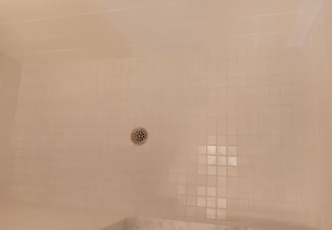 After Close-up of a clean white tiled shower floor with a central metal drain and clean grout lines visible.
