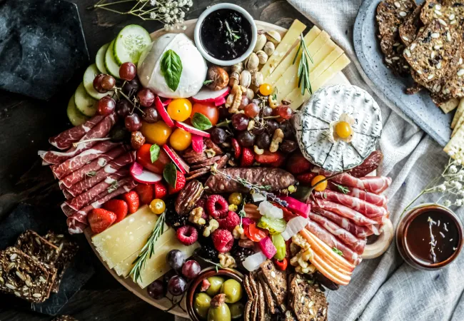 Gourmet charcuterie board with assorted cheeses, cured meats, fruits, nuts, olives, and crackers on a rustic table.