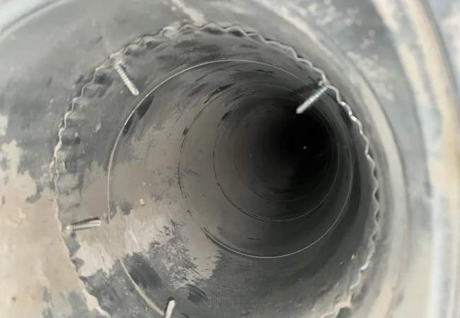 Close-up view inside a metal ventilation duct showing screws and a corrugated edge in a dusty environment