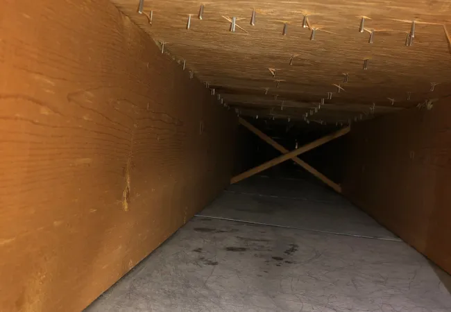 View inside a wooden box with staples on the top panel and a gray textured bottom surface extending inward.