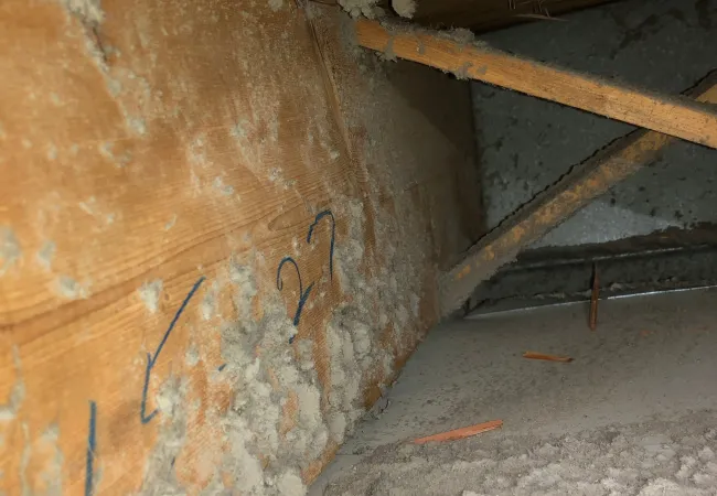 Dusty attic corner with wooden beams, insulation material, and metal support braces under a roof.