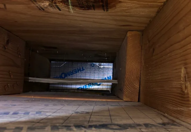 Interior view of a wooden framed wall cavity with insulation board and wiring visible.