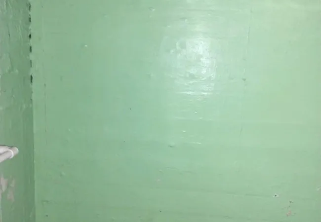 Green painted concrete basement wall with exposed pipe and rough ceiling texture in dim lighting.