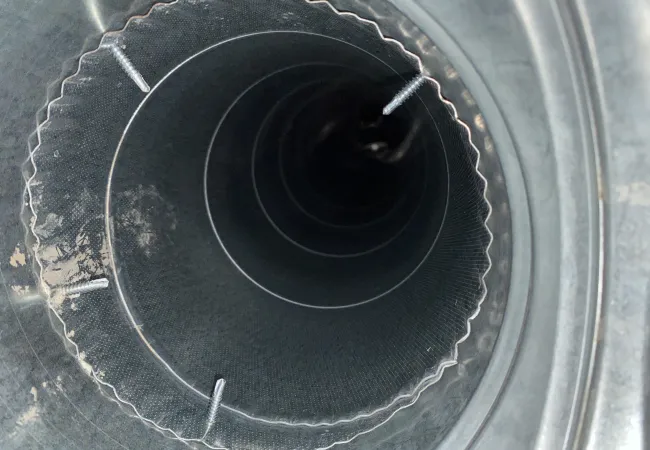 Close-up view inside a flexible metal duct with mesh lining and wire supports, used for ventilation.