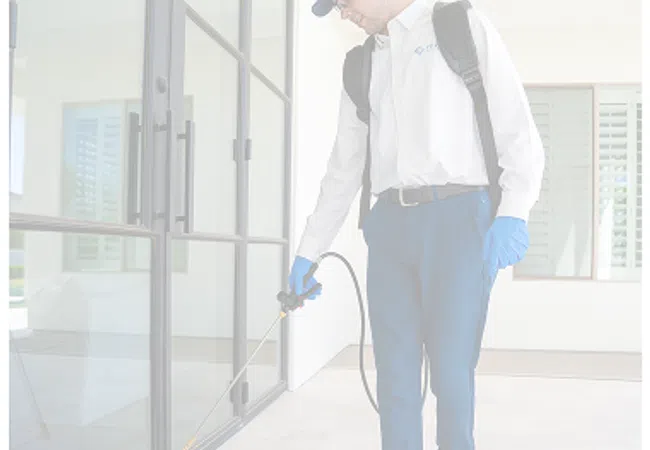 Pest control technician spraying insecticide along glass door frames at a residential property.