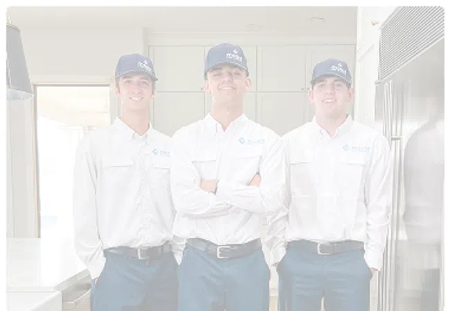 Three uniformed technicians wearing white shirts and blue pants standing in a modern kitchen.