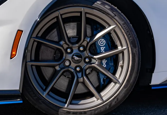 Close-up of a sleek black alloy wheel with Brembo brake caliper on a white sports car on asphalt.