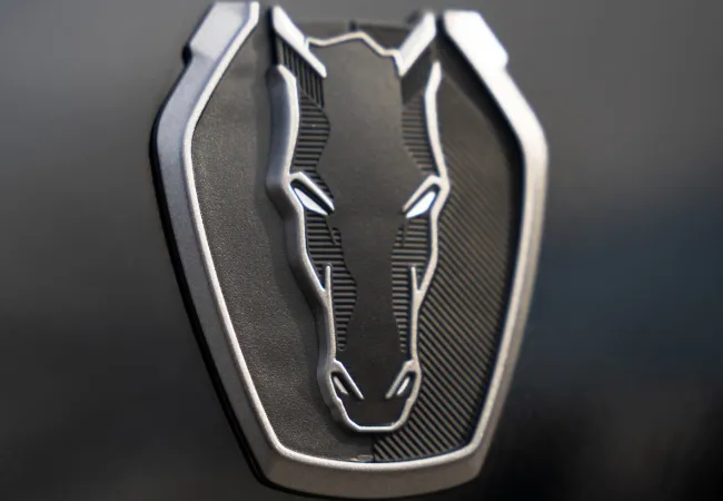 Close-up of a metallic horse head emblem with a shield-shaped background on a black surface.