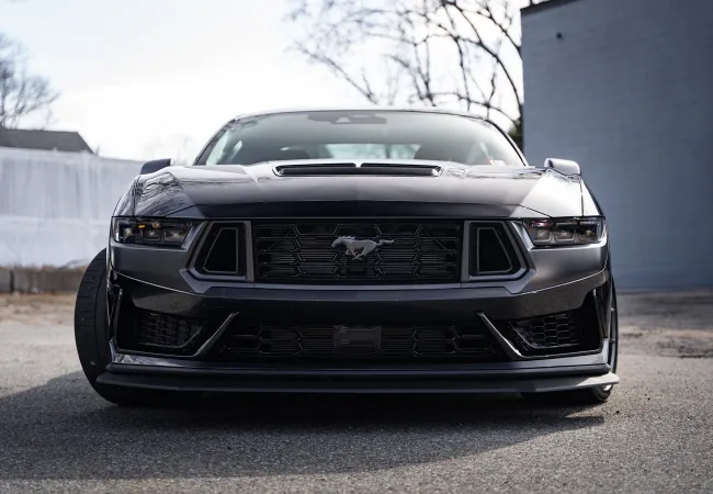Front view of a sleek black Ford Mustang parked outdoors with a glossy finish and aggressive design.