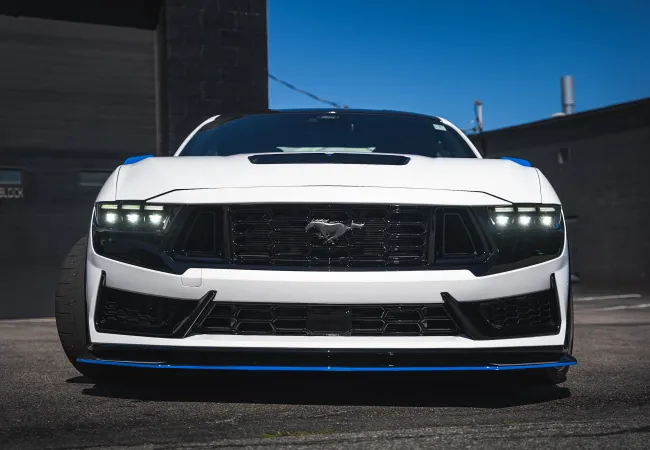 Front view of a white Ford Mustang with aggressive LED headlights and a black grille featuring the Mustang emblem.