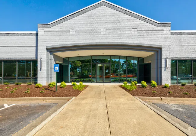 Modern commercial building entrance with glass doors, landscaped garden, and blue sky in background