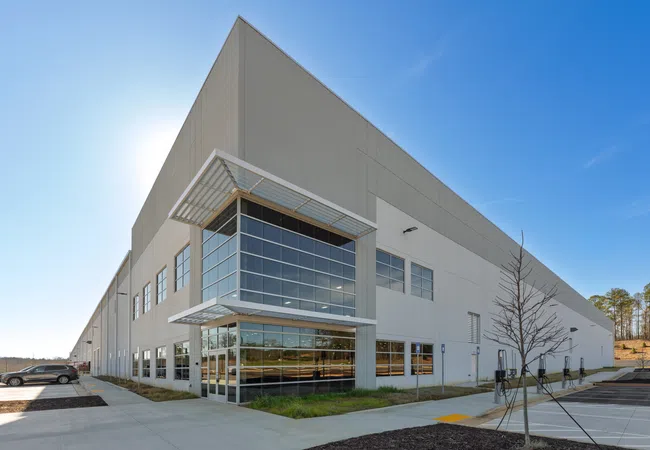 Large modern warehouse building with glass entrance under a clear blue sky and surrounding parking lot.